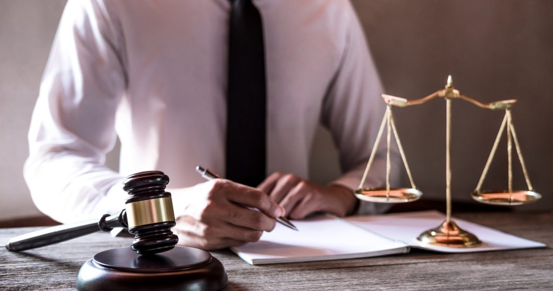 Legal law, advice and justice concept, Professional male lawyers working on courtroom sitting at the table and signing papers with gavel and Scales of justice.